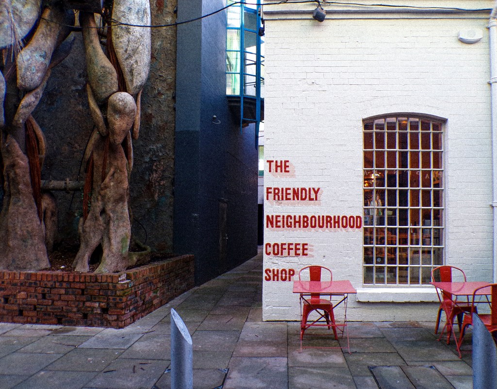 a coffee shop with a white wall, and a red logo on the front saying 'the friendly neighbourhood coffee shop'
