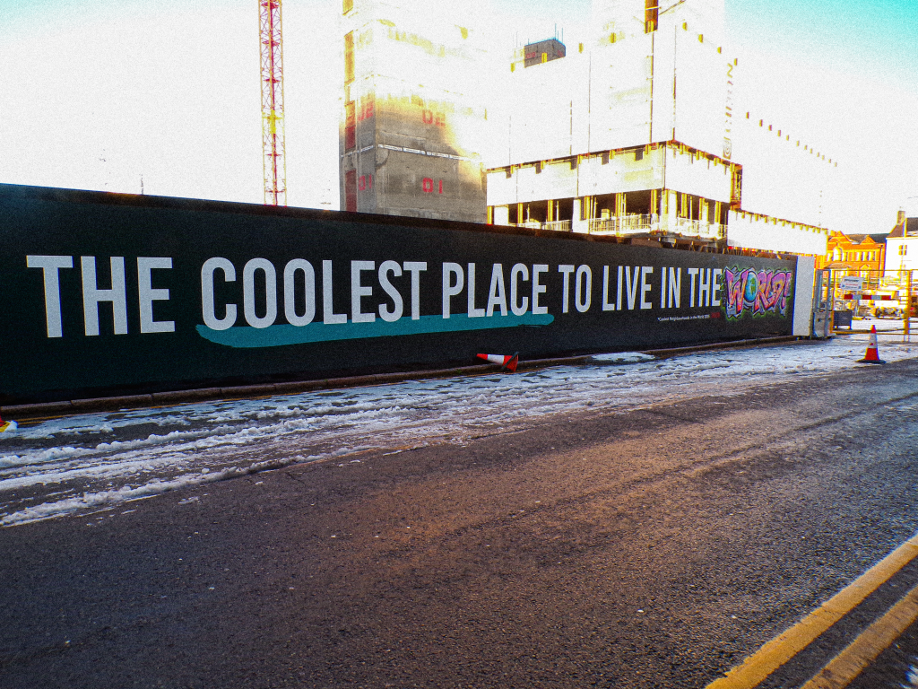 a sign in front of a development of high rise flats that says 'the coolest place to live in the world'